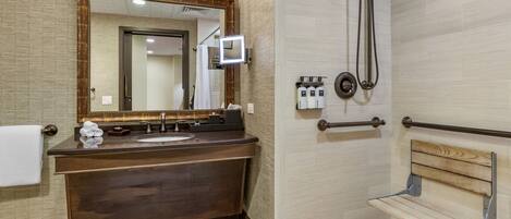 Een moderne badkamer met een donker houten wastafelmeubel, een grote spiegel, een douche met handdouche en een houten bankje.
