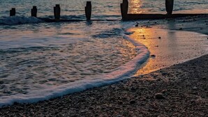 A beach with waves at sunset, a clear sky, and a row of stone pillars. - The Langstone Quays (Hayling Island)