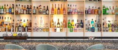 Zona de bar con varias estanterías llenas de botellas, una barra y taburetes.