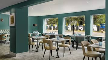 A modern dining area with teal walls, large windows, and a mix of round and rectangular tables.