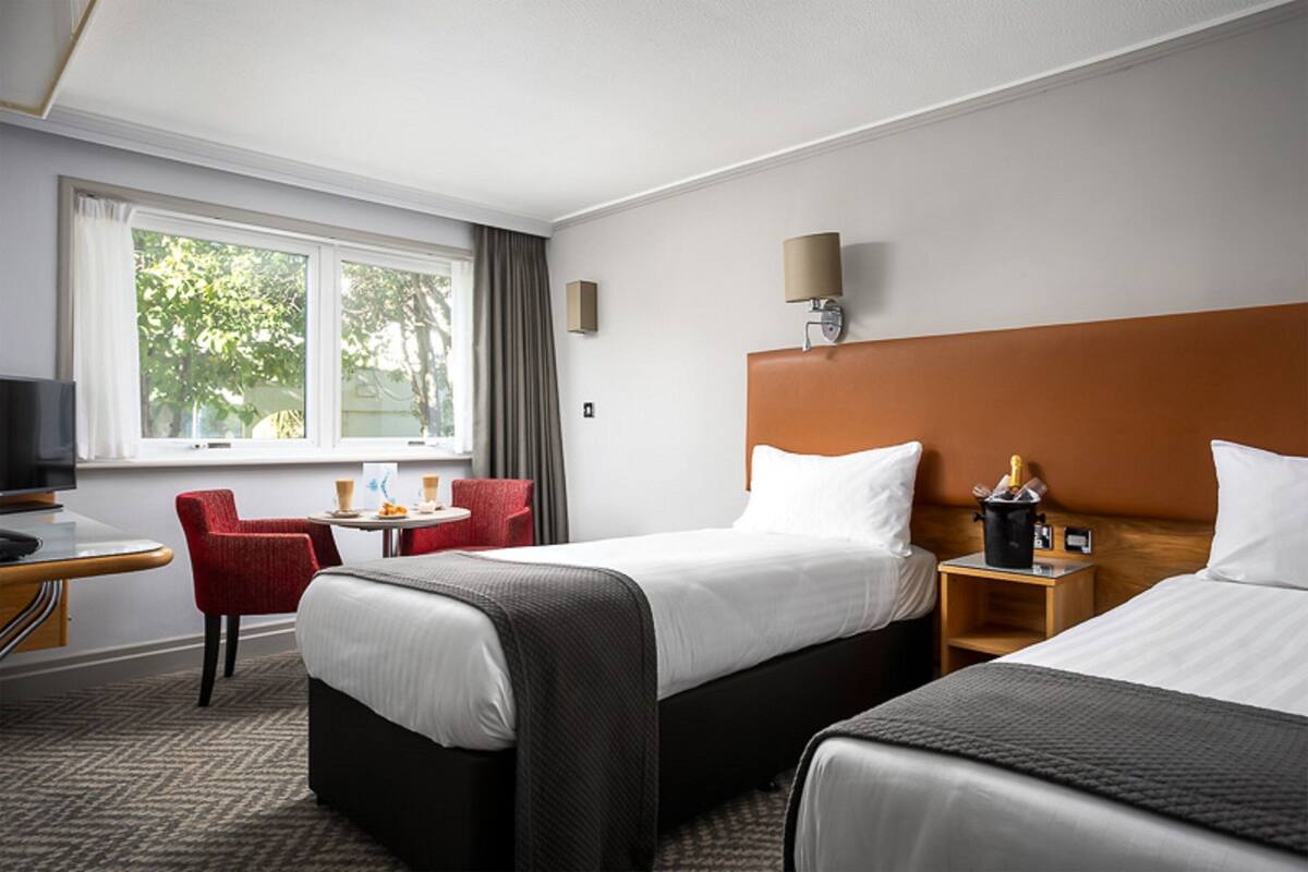 A hotel room with two beds, a desk, a chair, a TV, and a window with curtains.