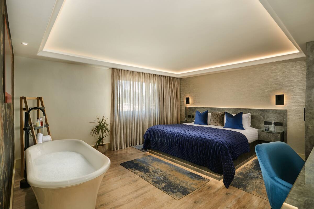 A modern bedroom with a large bed, a bathtub, and a nightstand with a lamp.