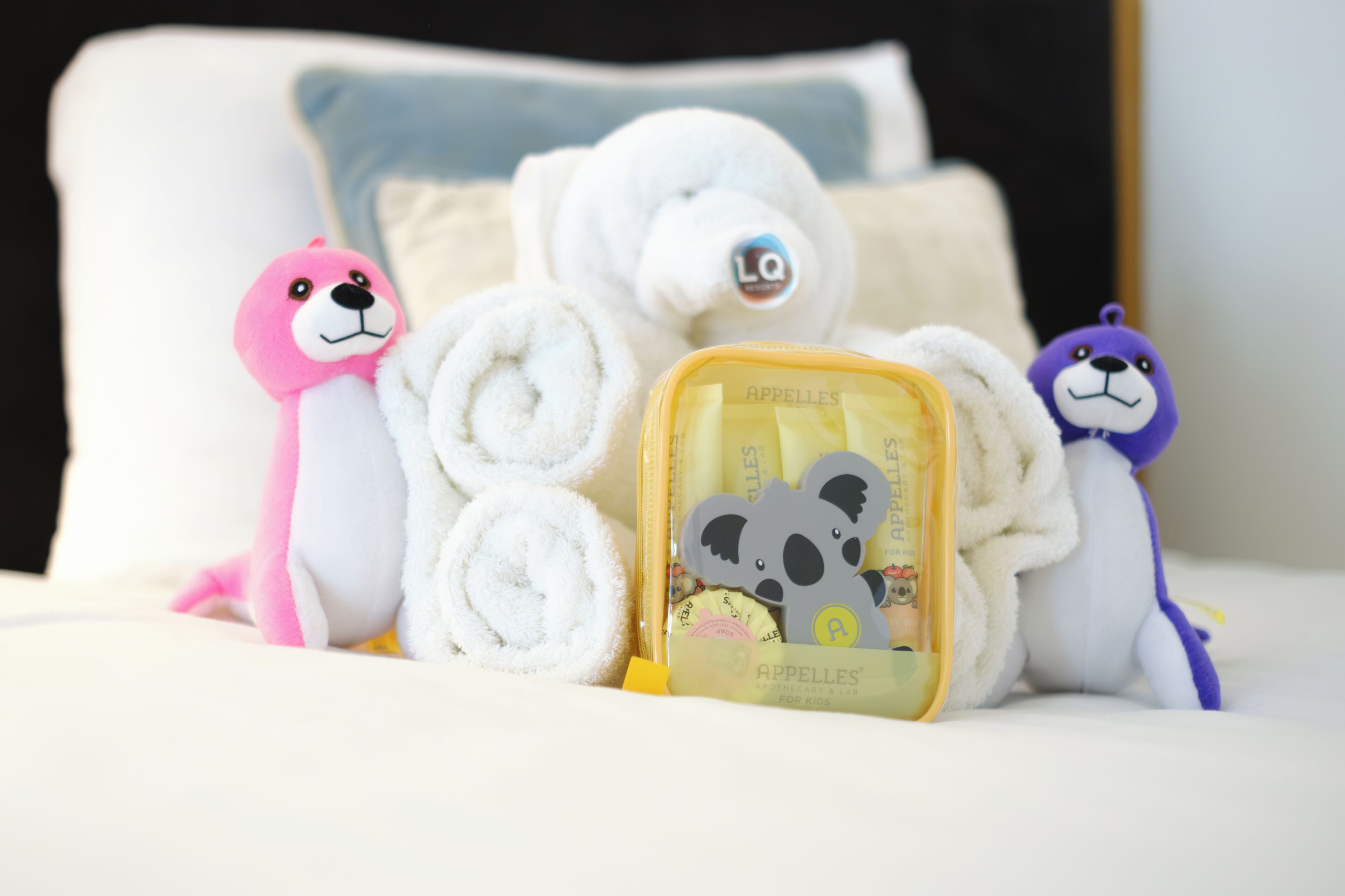 A bed with rolled towels, a plush toy, and a small box with a bear design.