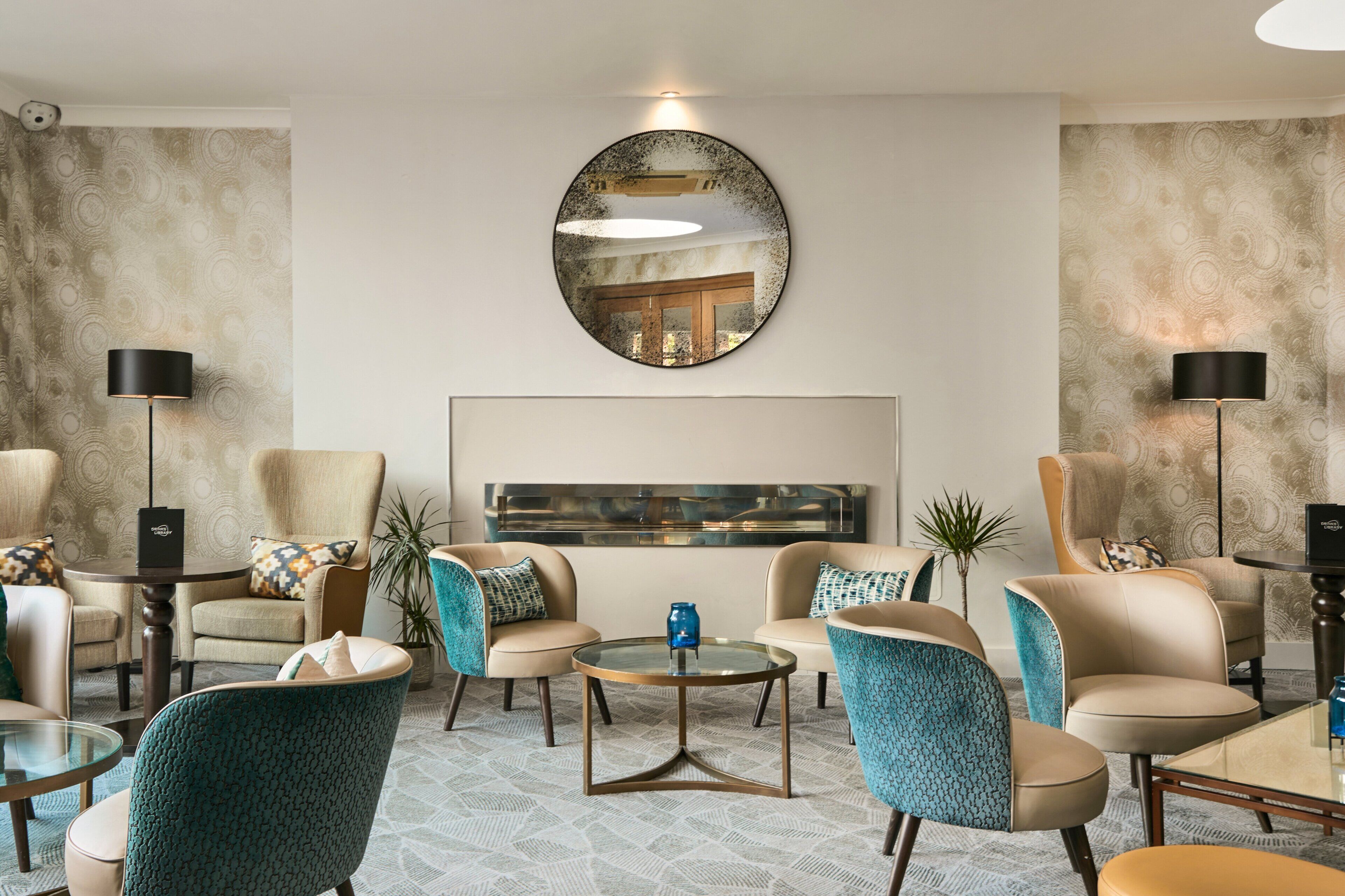 A modern lounge area with leather armchairs, a glass coffee table, and a large mirror on the wall.