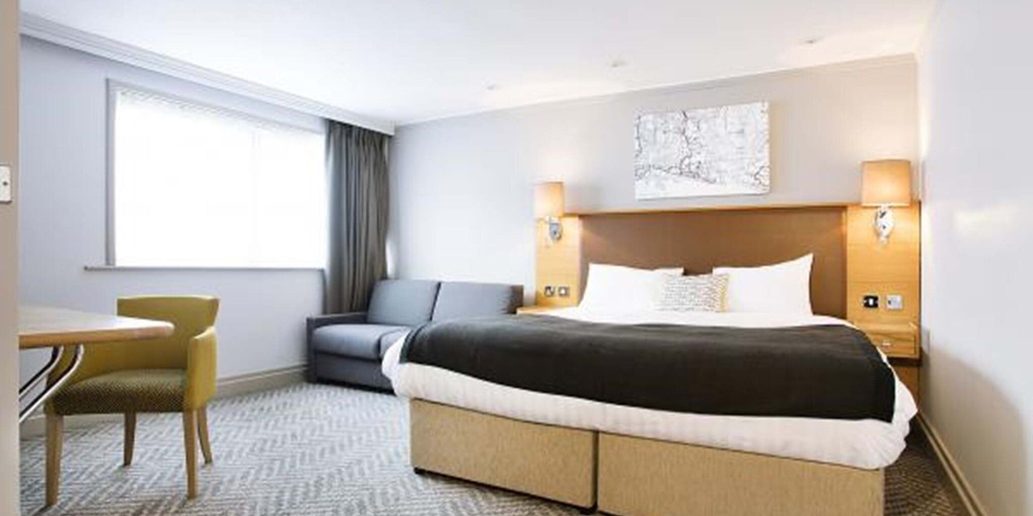 Habitación de hotel con una cama, un escritorio, una silla y un ventanal grande.