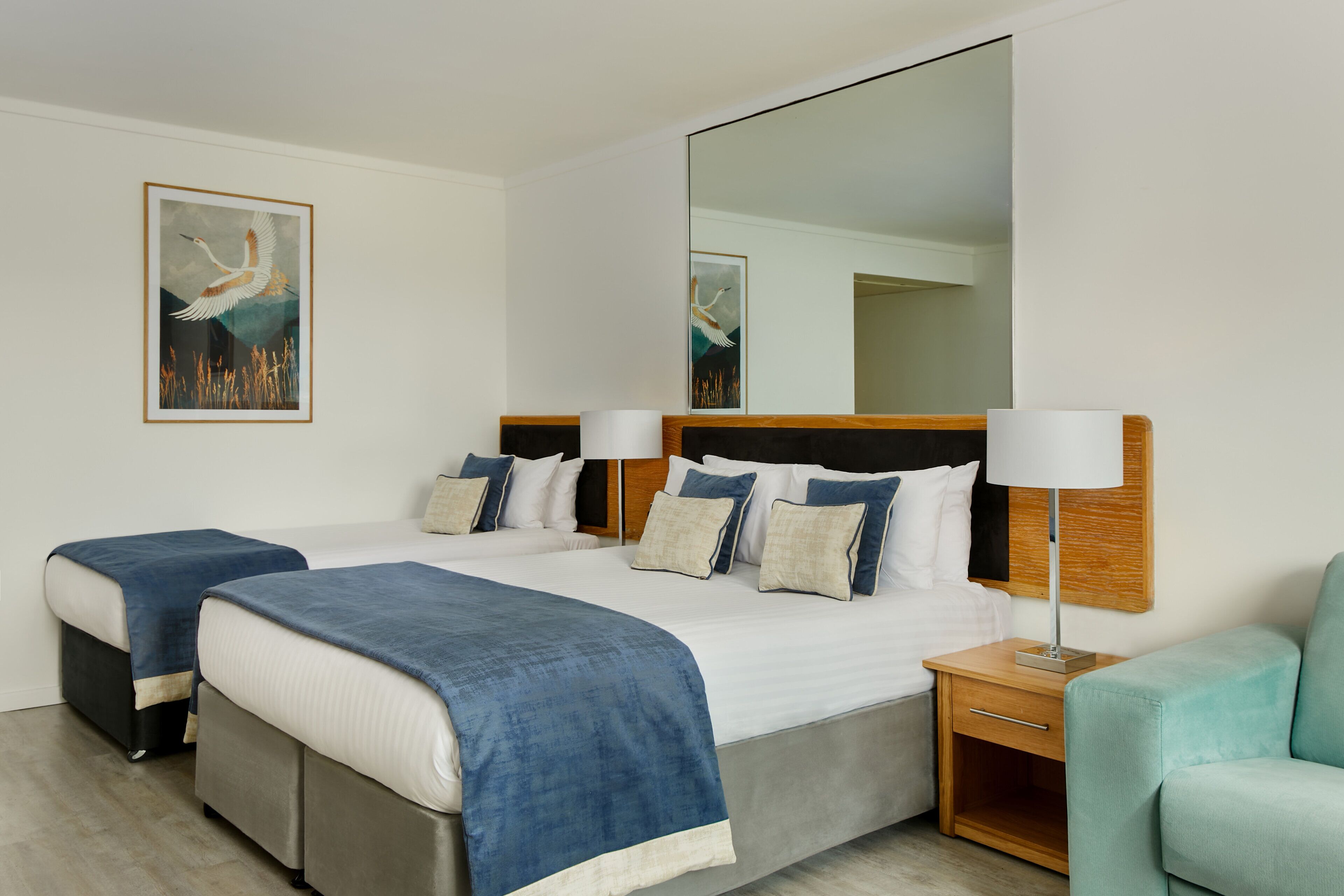 Habitación de hotel con una cama grande, dos mesitas de noche, un espejo y una obra de arte enmarcada en la pared.