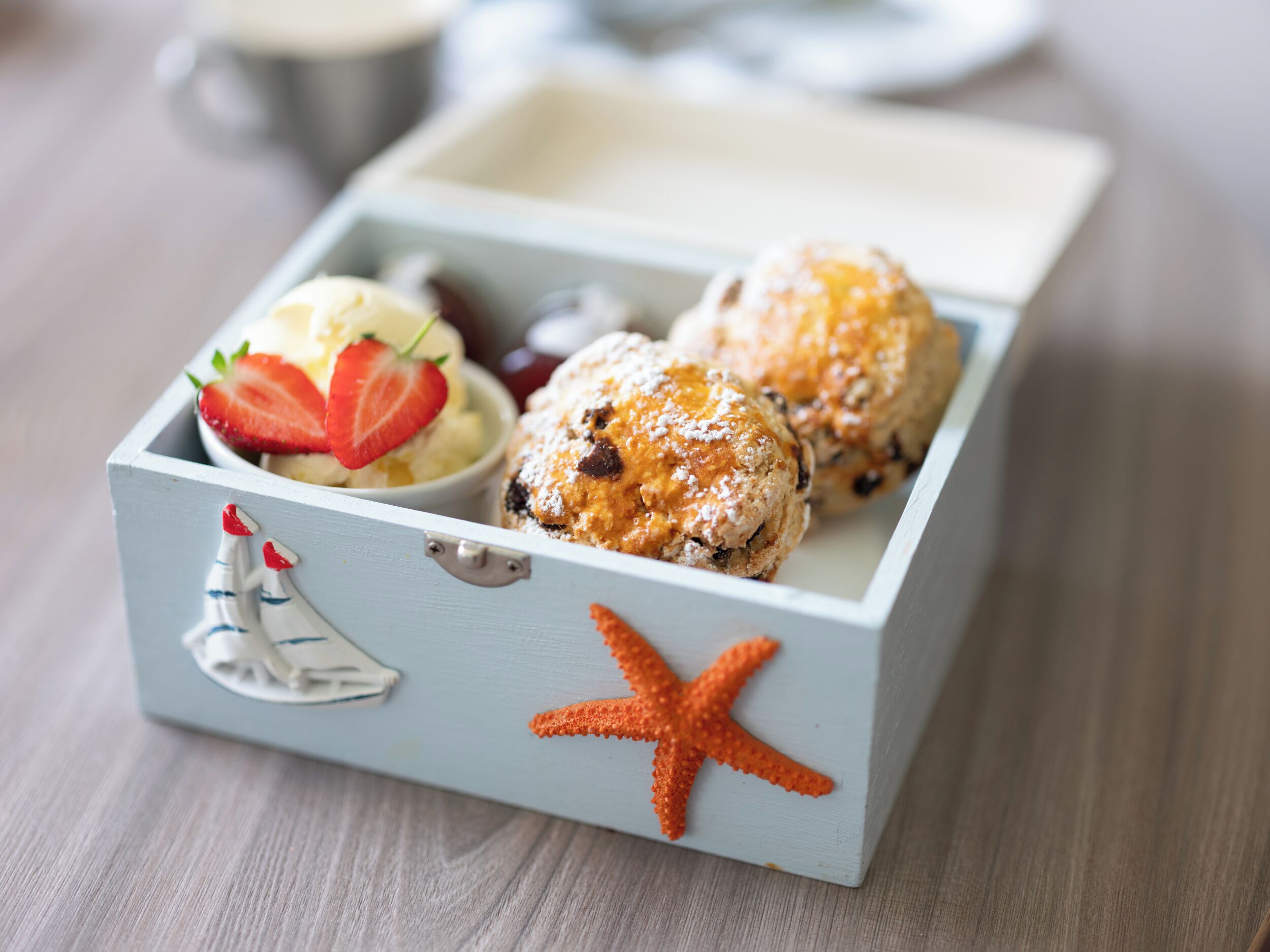 A wooden box with a nautical theme, containing pastries and a bowl of ice cream with strawberries.