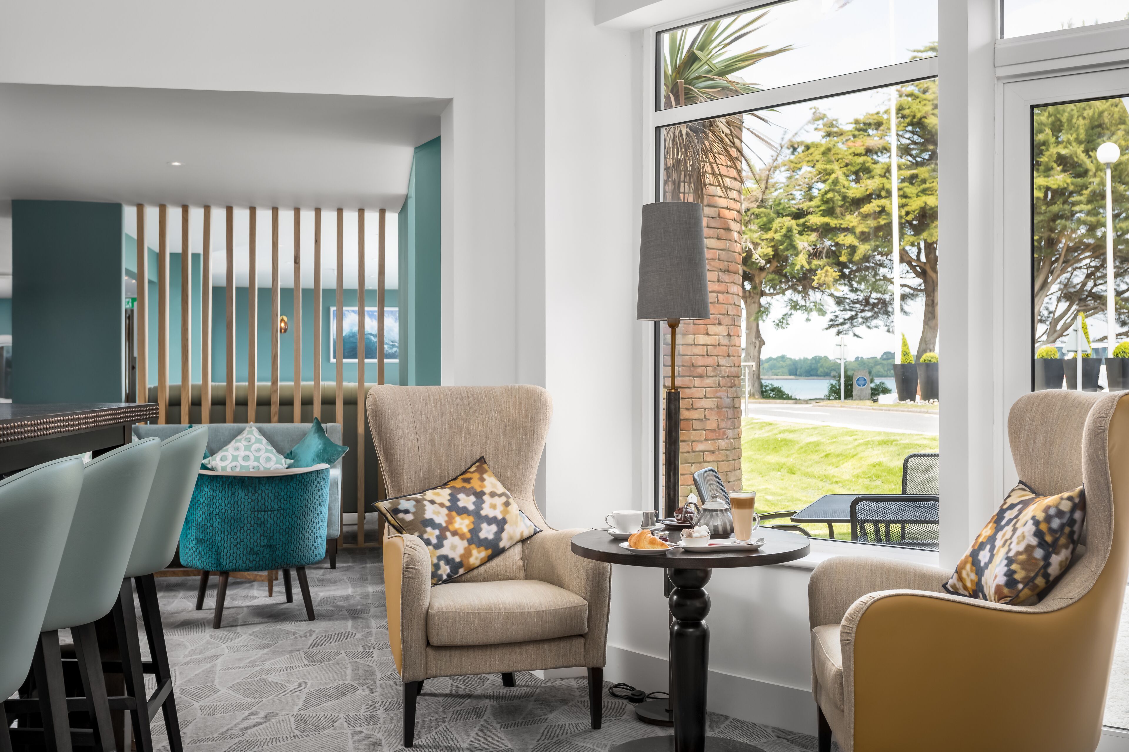 A modern lounge area with a bar, comfortable seating, and a large window offering a view of the outdoors.