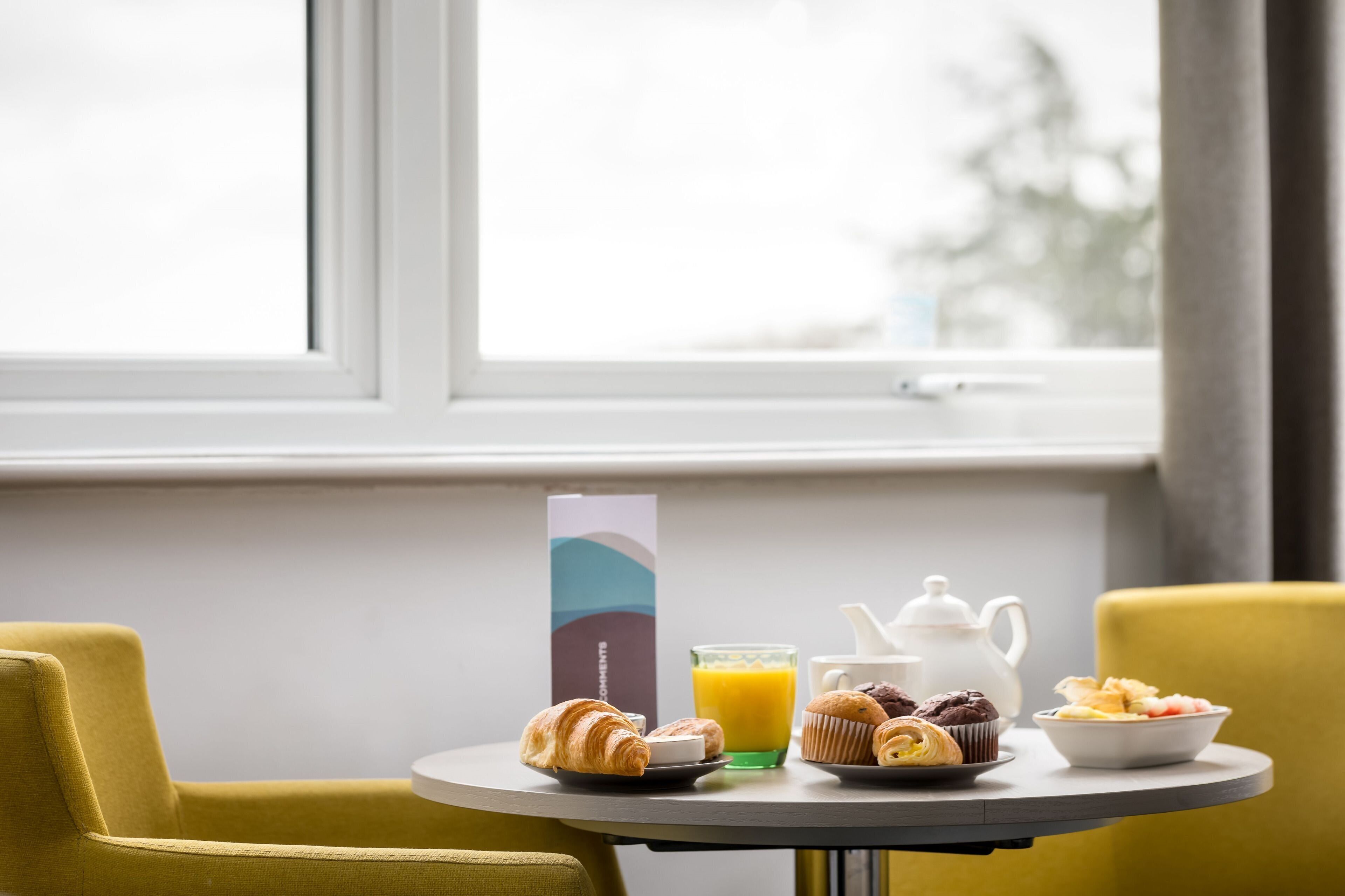 A breakfast table with croissants, muffins, a jug of orange juice, and a teapot.