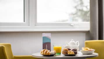 Une table de petit-déjeuner avec des croissants, des muffins, un pichet de jus d’orange et une théière.