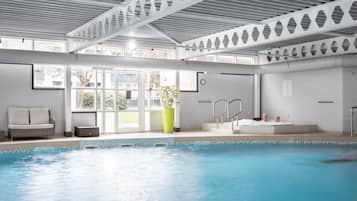 An indoor swimming pool with a clear view of the outside, a seating area with a sofa, and a hot tub.