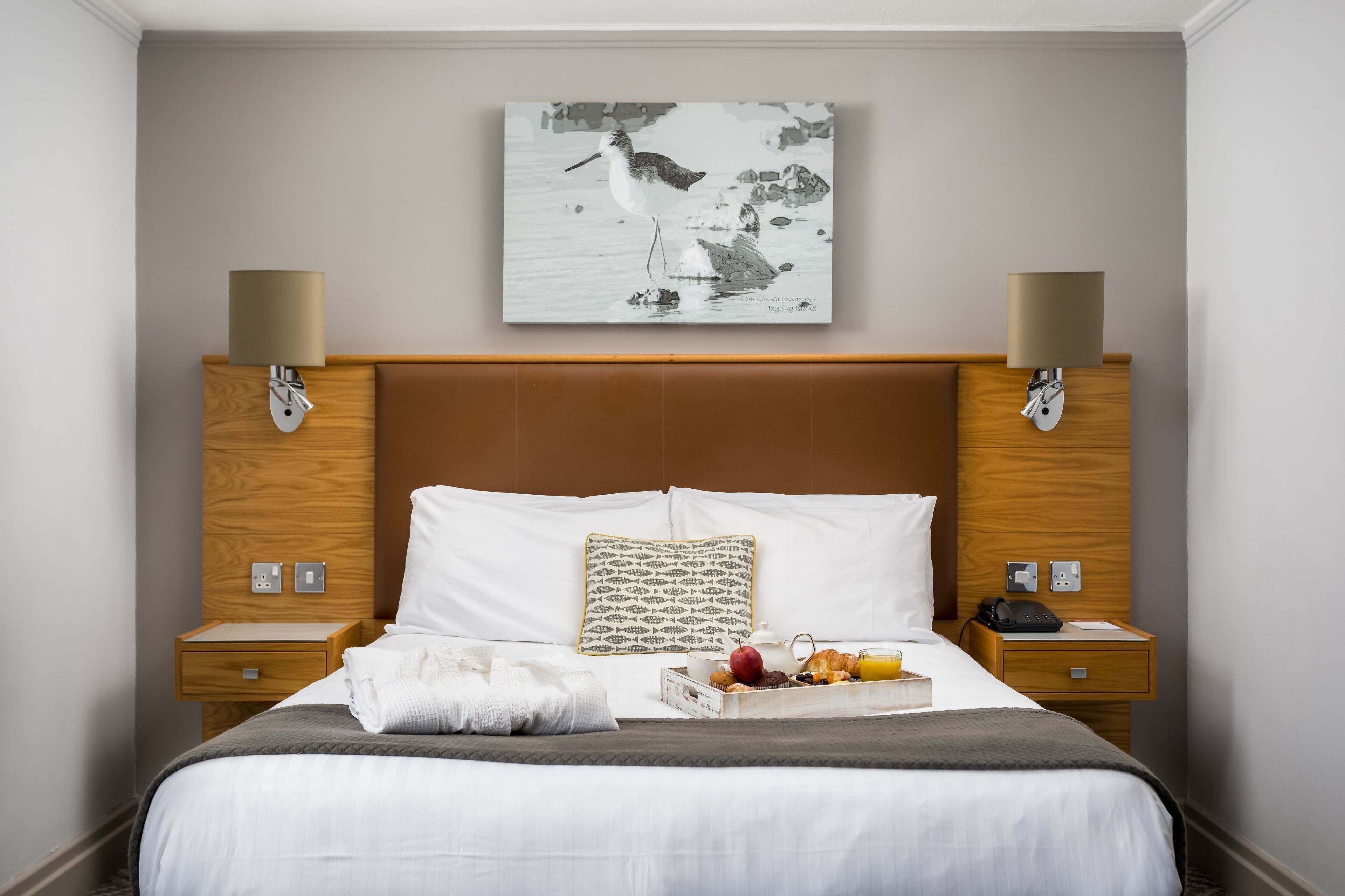A neatly made bed with a tray of breakfast, a pillow, and a wall-mounted artwork.