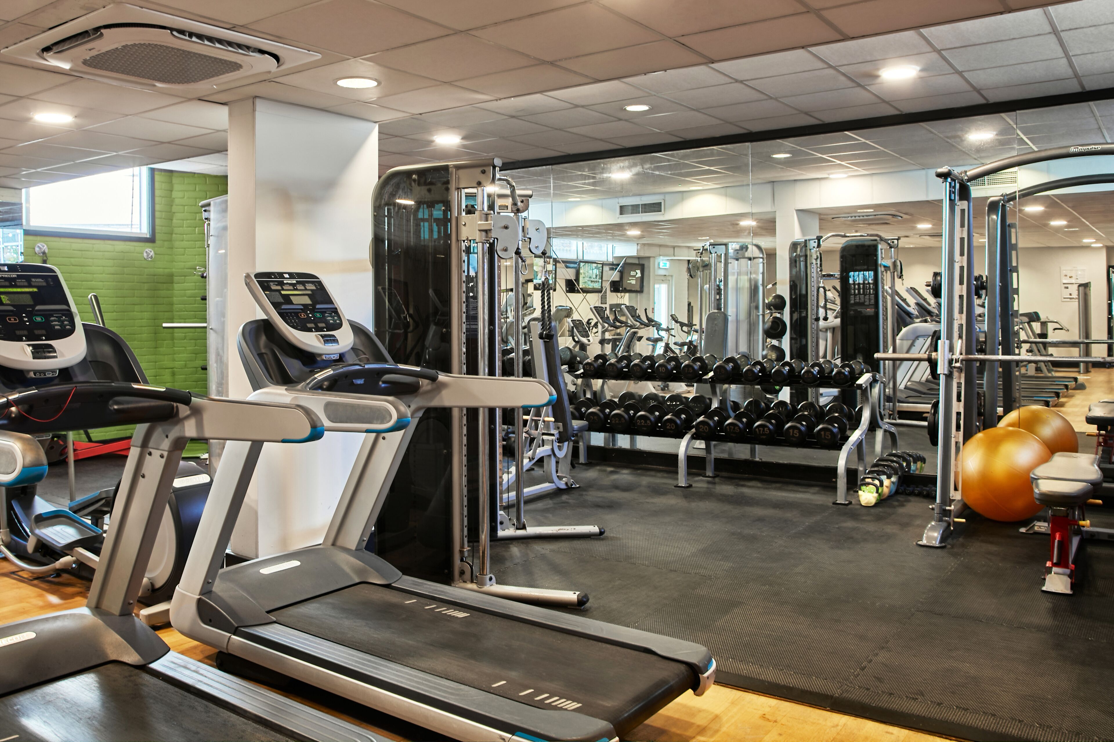 Et fitnesscenter med løbebånd, træningsmaskiner og en vægtstang med håndvægte.