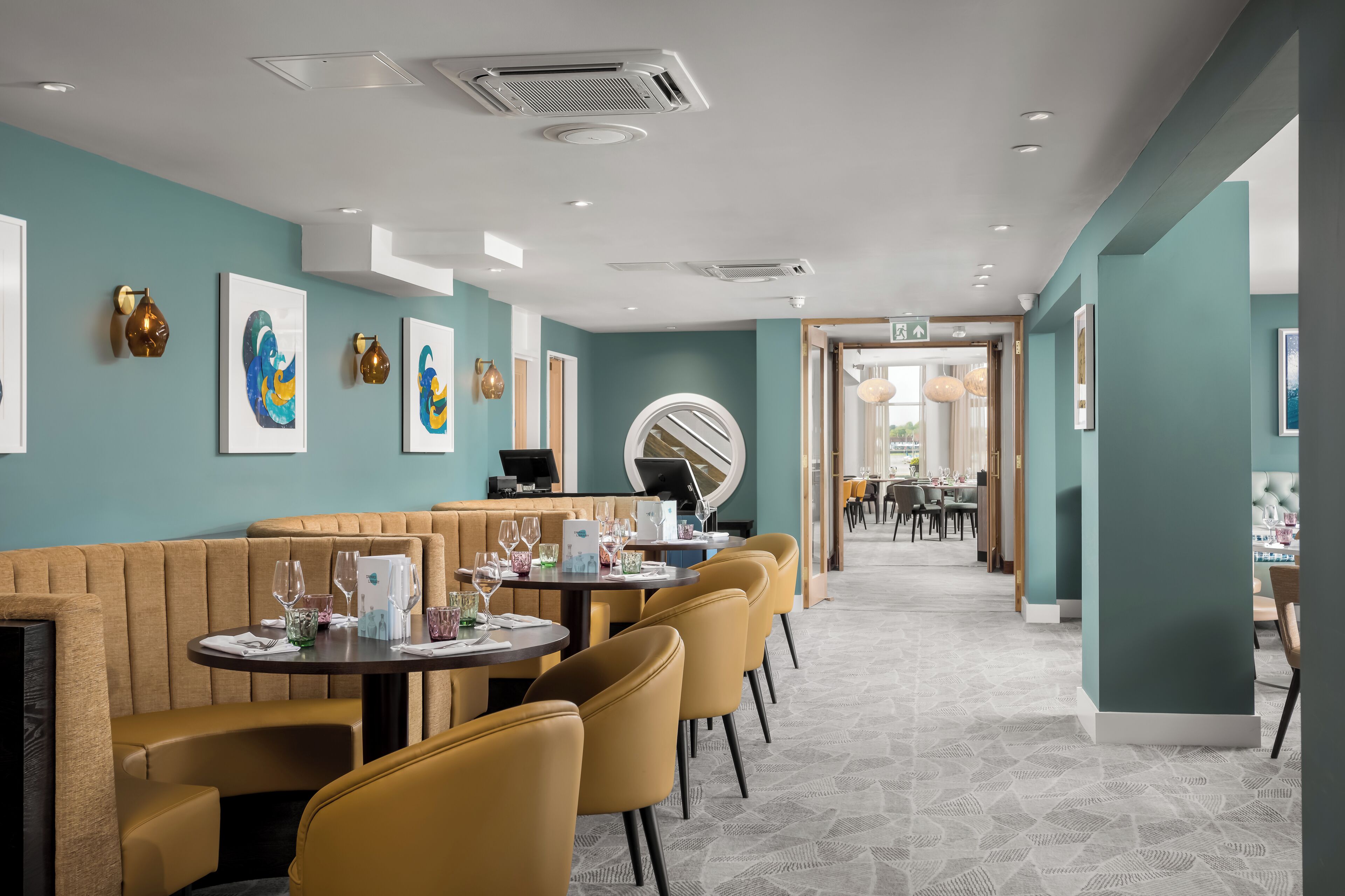 Un restaurante moderno con paredes color turquesa, asientos tipo cabina de madera y piso estampado.