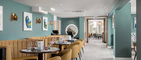 Un restaurante moderno con paredes color turquesa, asientos tipo cabina de madera y piso estampado.