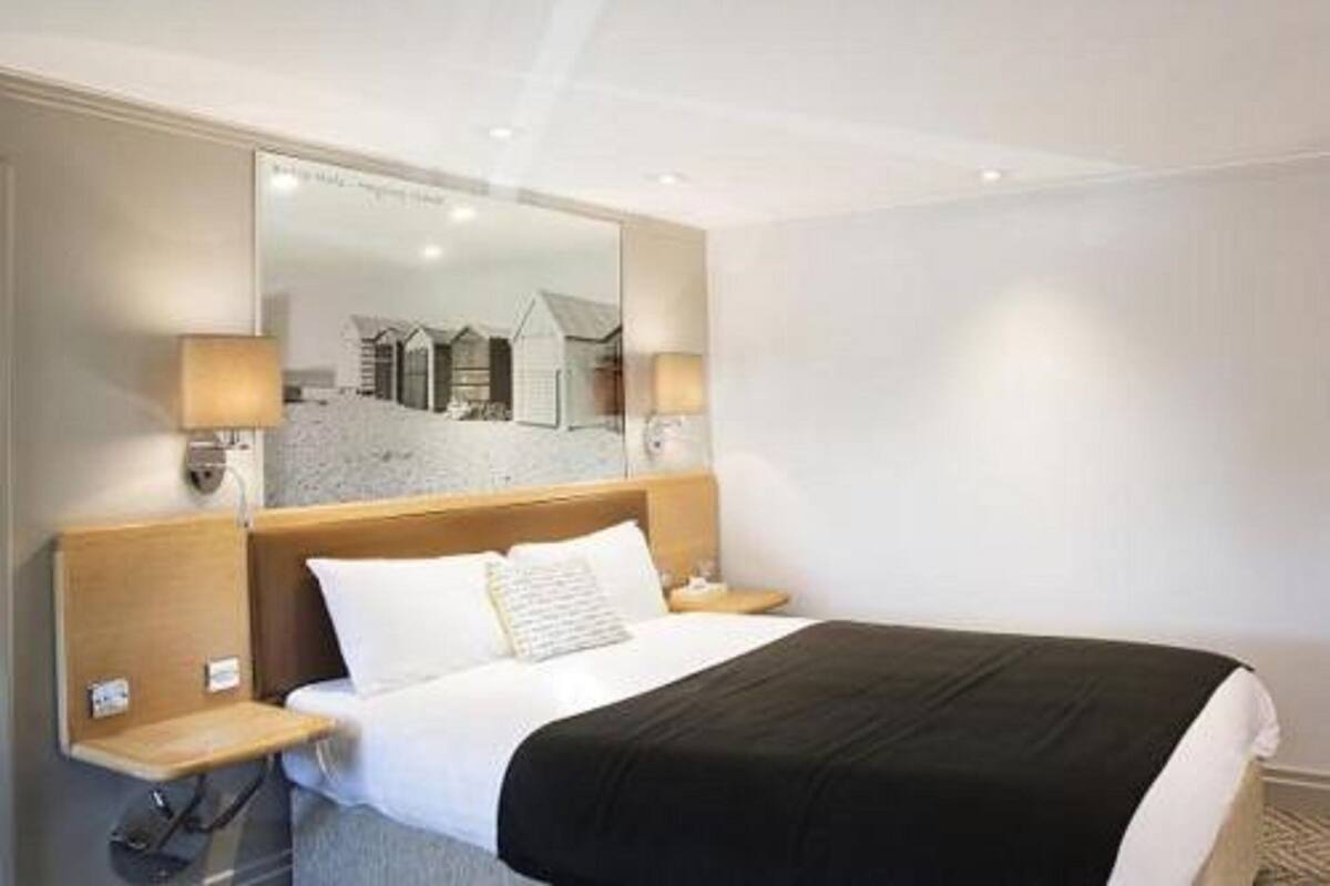 A hotel room with a large bed, a nightstand, a mirror, and a view of a beach through the window.