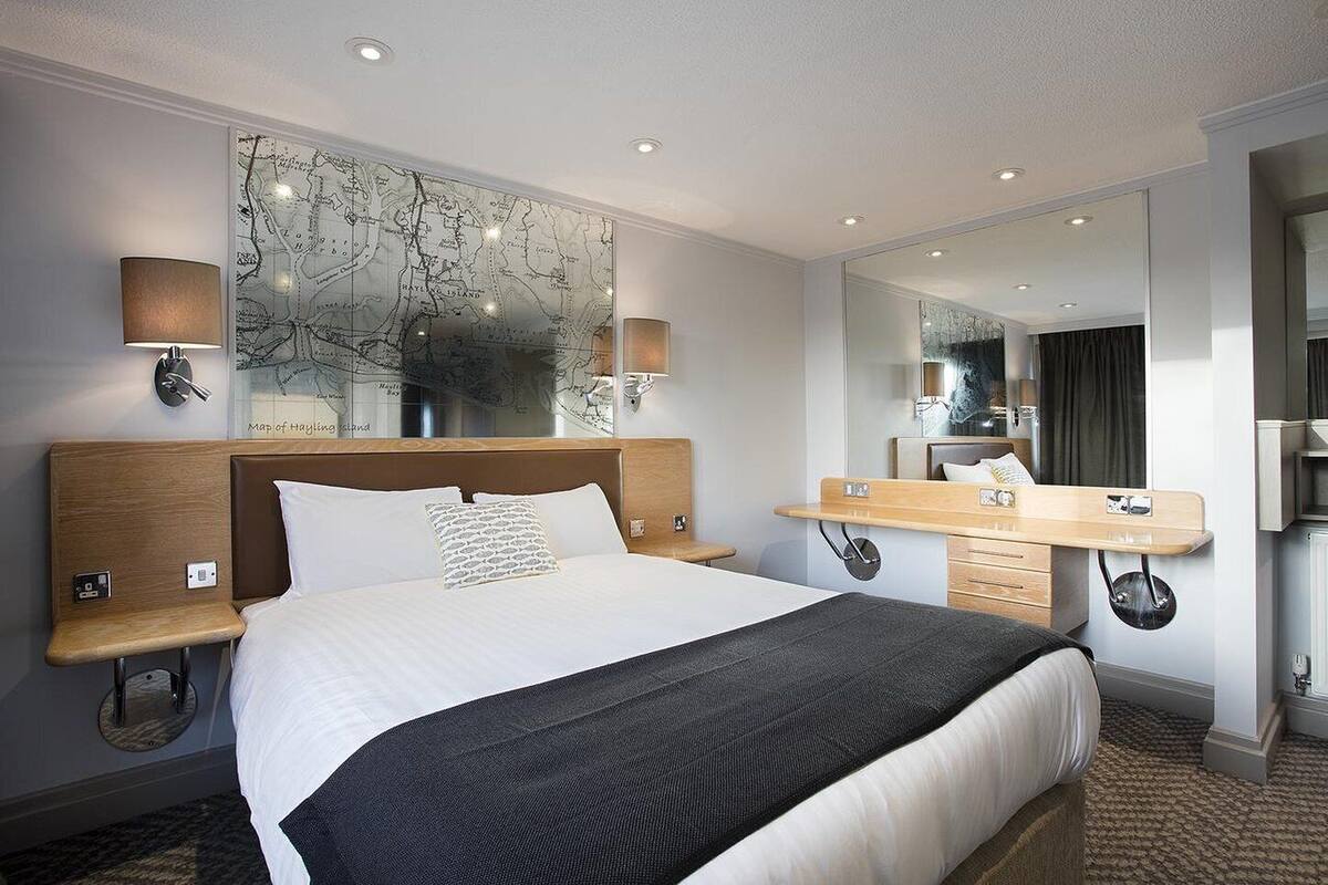 A hotel room with a large bed, a wooden headboard, a map on the wall, a bedside table with a lamp, and a mirror.