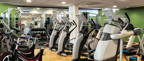 A gym with various cardio machines, weightlifting equipment, and a mirrored wall.