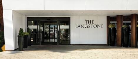 Ingången till hotellet The Langstone, med en modern fasad, glasdörrar och krukväxter.