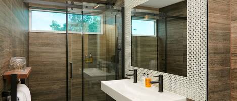 Un baño moderno con cabina de ducha de vidrio, un espejo grande y un lavabo blanco.