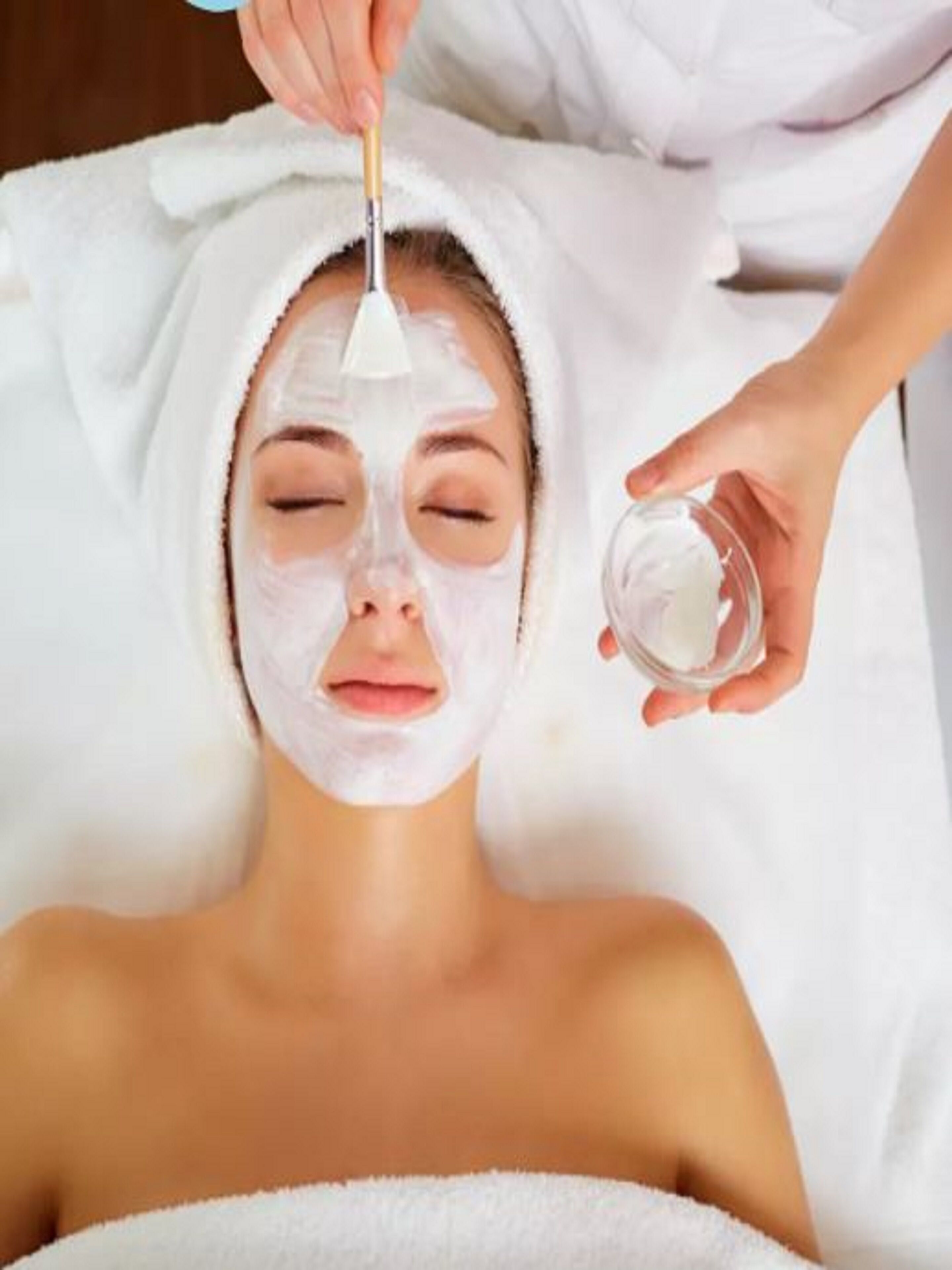 A person receiving a facial treatment with a white towel wrapped around their head.