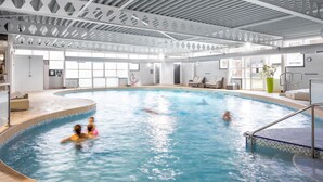 An indoor swimming pool with clear water, surrounded by a modern architectural design with geometric patterns on the ceiling and walls. - The Langstone Quays (Hayling Island)