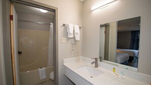 Ein Badezimmer mit einer Badewanne, einem Waschbecken und einem Spiegel. Handtücher hängen an der Wand und eine Duschvorhang ist angebracht.