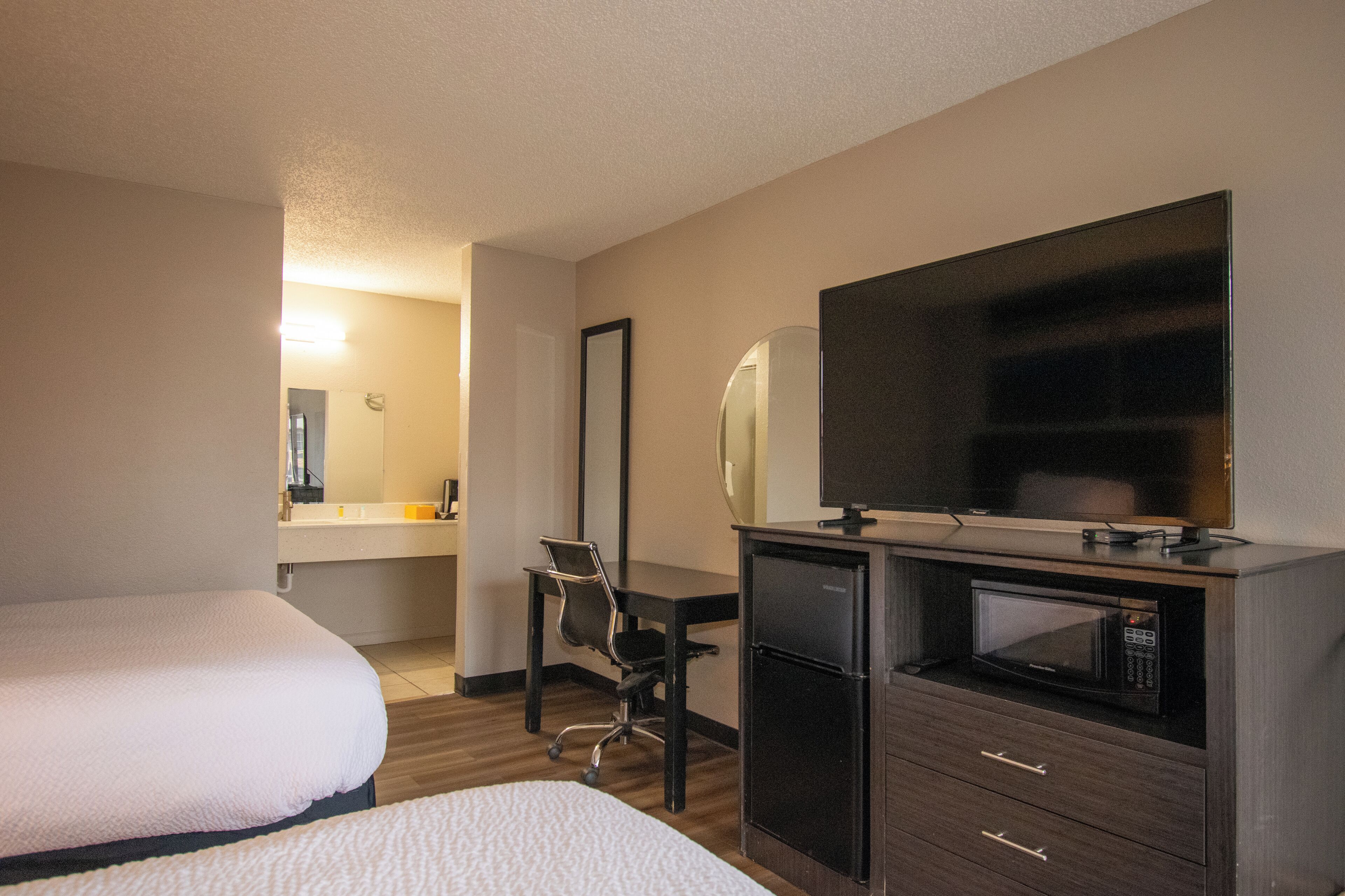 A hotel room with two beds, a desk, a chair, a mirror, a television, and a microwave.