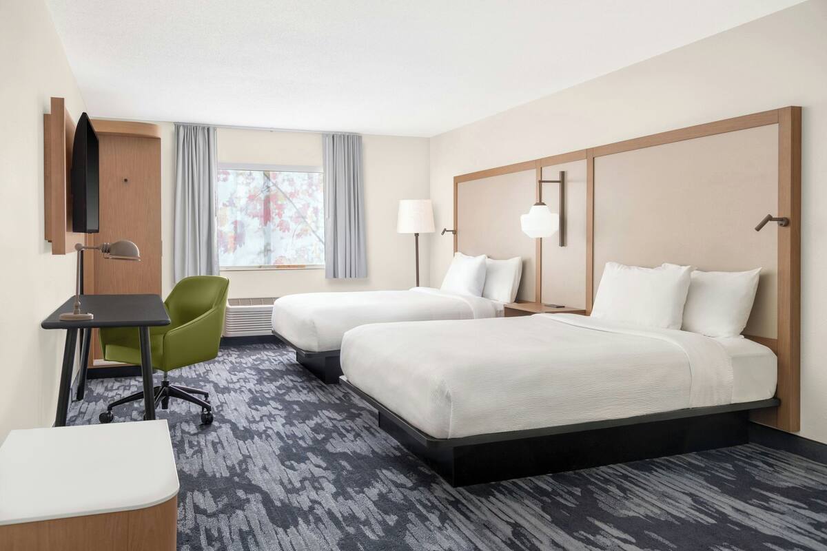 A hotel room with two beds, a desk, a chair, a TV, and a window with curtains.