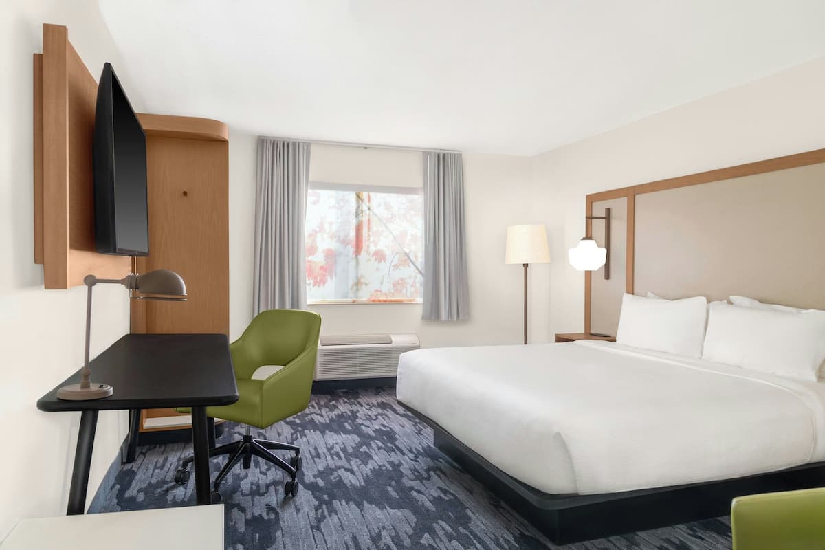 A hotel room with a bed, a desk, a chair, a TV, and a window with curtains.