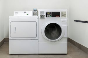 Una lavadora y secadora apilables con pantalla digital y panel de control, ubicadas en una esquina con piso de baldosas y pared lisa.