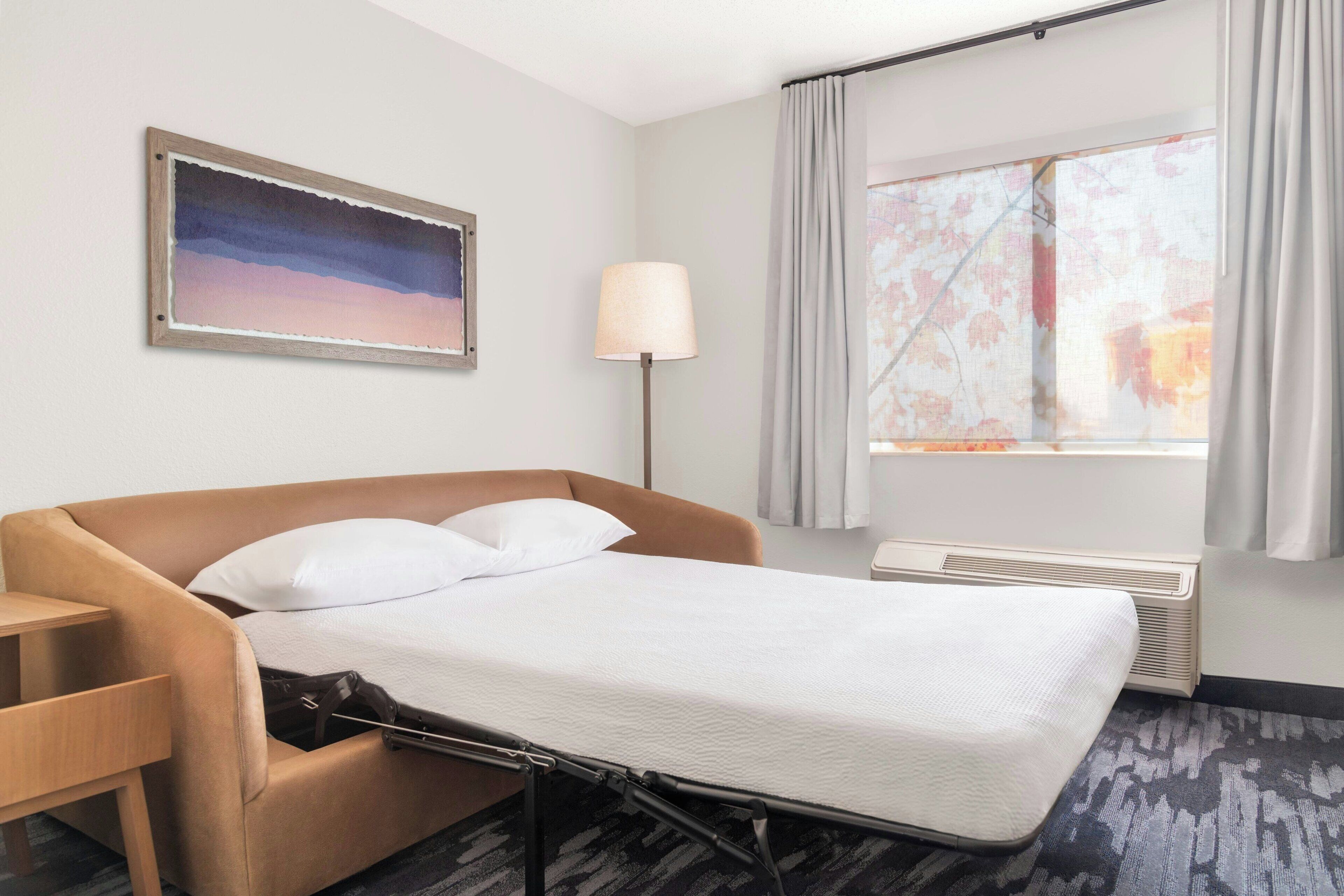 A hotel room with a bed, a desk, a lamp, and a window with curtains.