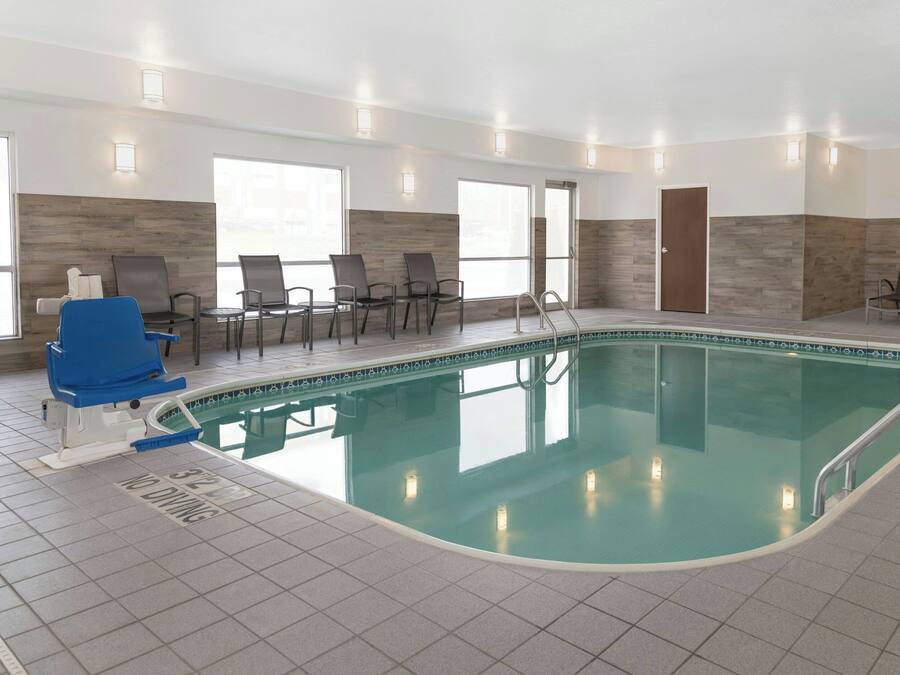 Piscina interior com plataforma de mergulho de 32 metros, rodeada por cadeiras e uma parede de madeira.