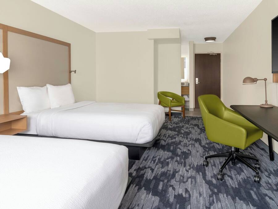 Habitación de hotel con dos camas, un escritorio, una silla verde, una lámpara y un televisor.