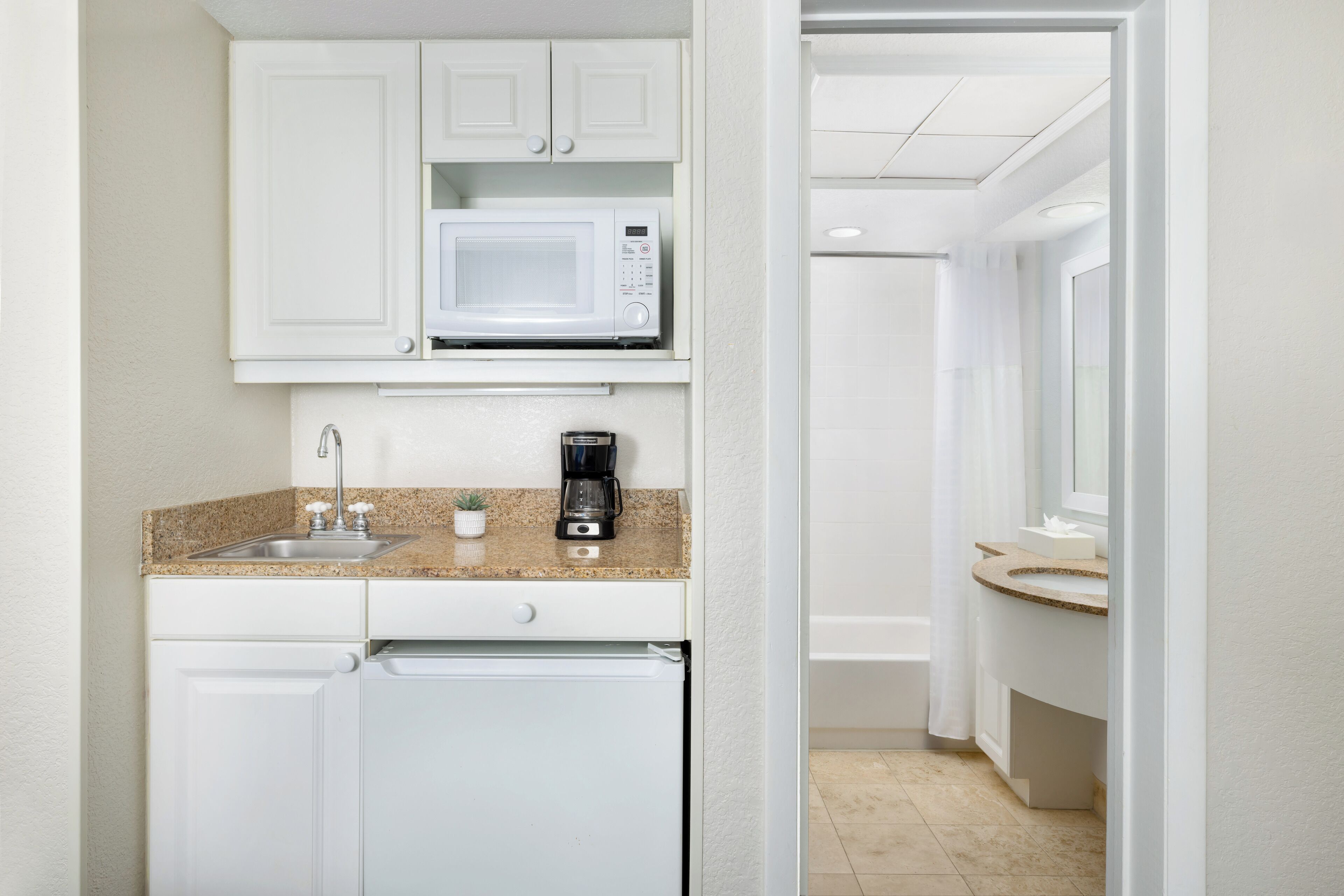 A compact kitchen with white cabinets, a microwave, a coffee maker, and a dishwasher.