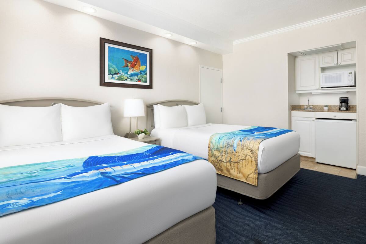 A hotel room with two beds, a kitchenette, and a framed picture on the wall.