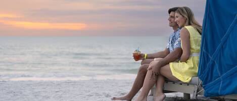 A couple sitting on a beach chair with a view of the ocean and a sunset.