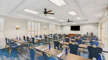 A conference room with multiple tables and chairs, ceiling fans, and wall-mounted televisions.