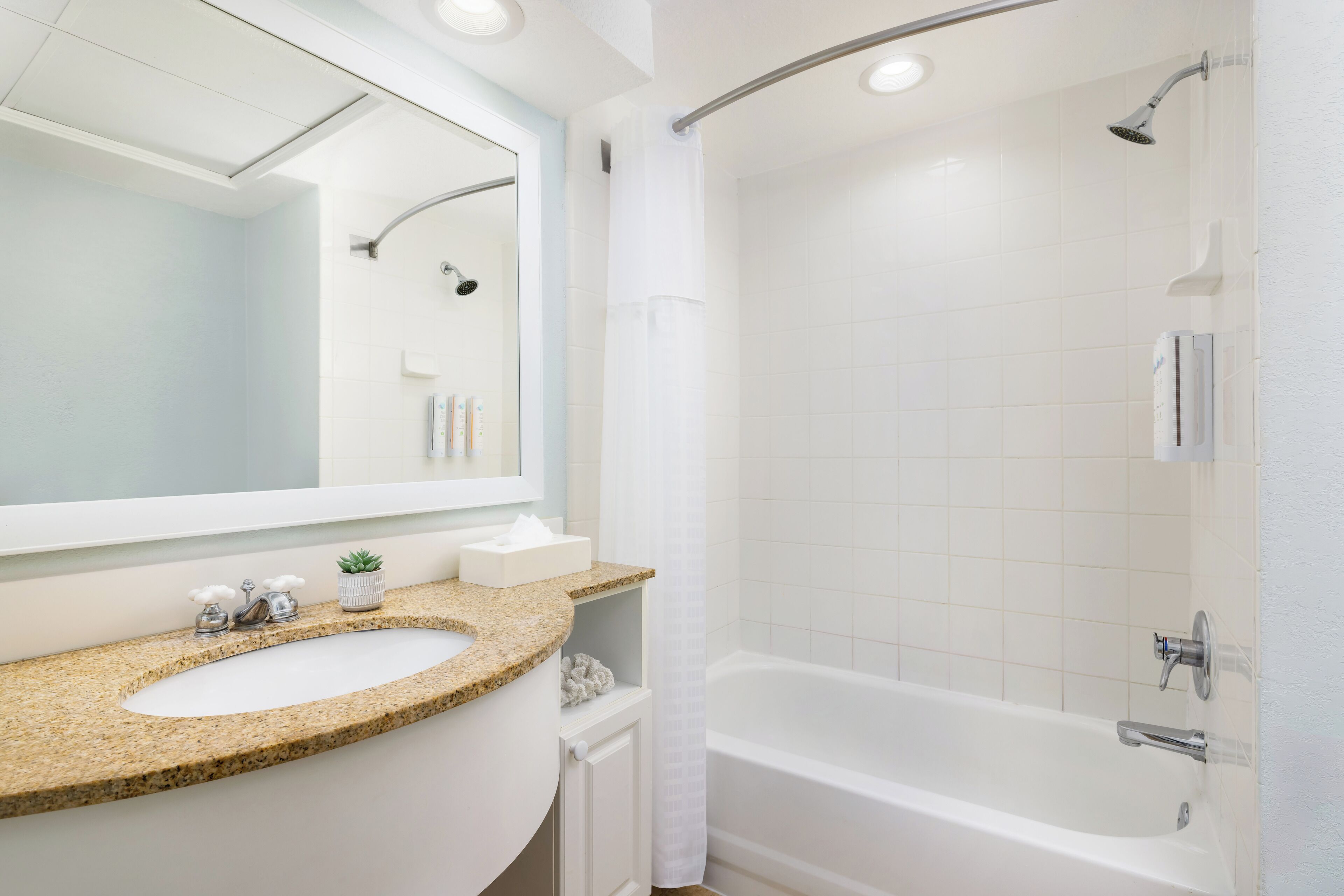 Un baño moderno con lavamanos de granito, un espejo grande, una bañera y una zona de ducha.