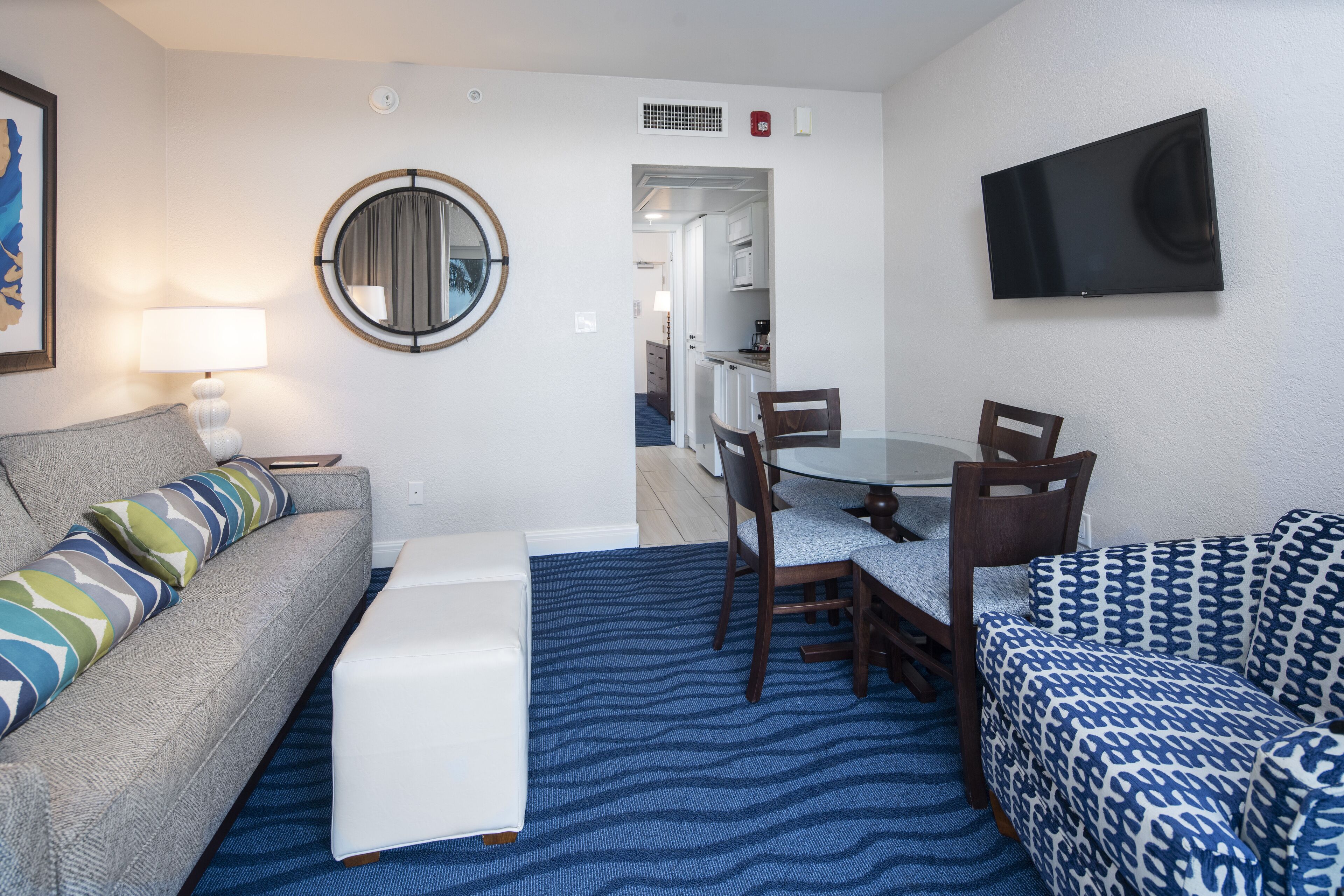 A compact hotel room with a sofa, a small table, a TV mounted on the wall, and a mirror.