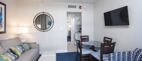 A compact hotel room with a sofa, a small table, a TV mounted on the wall, and a mirror.