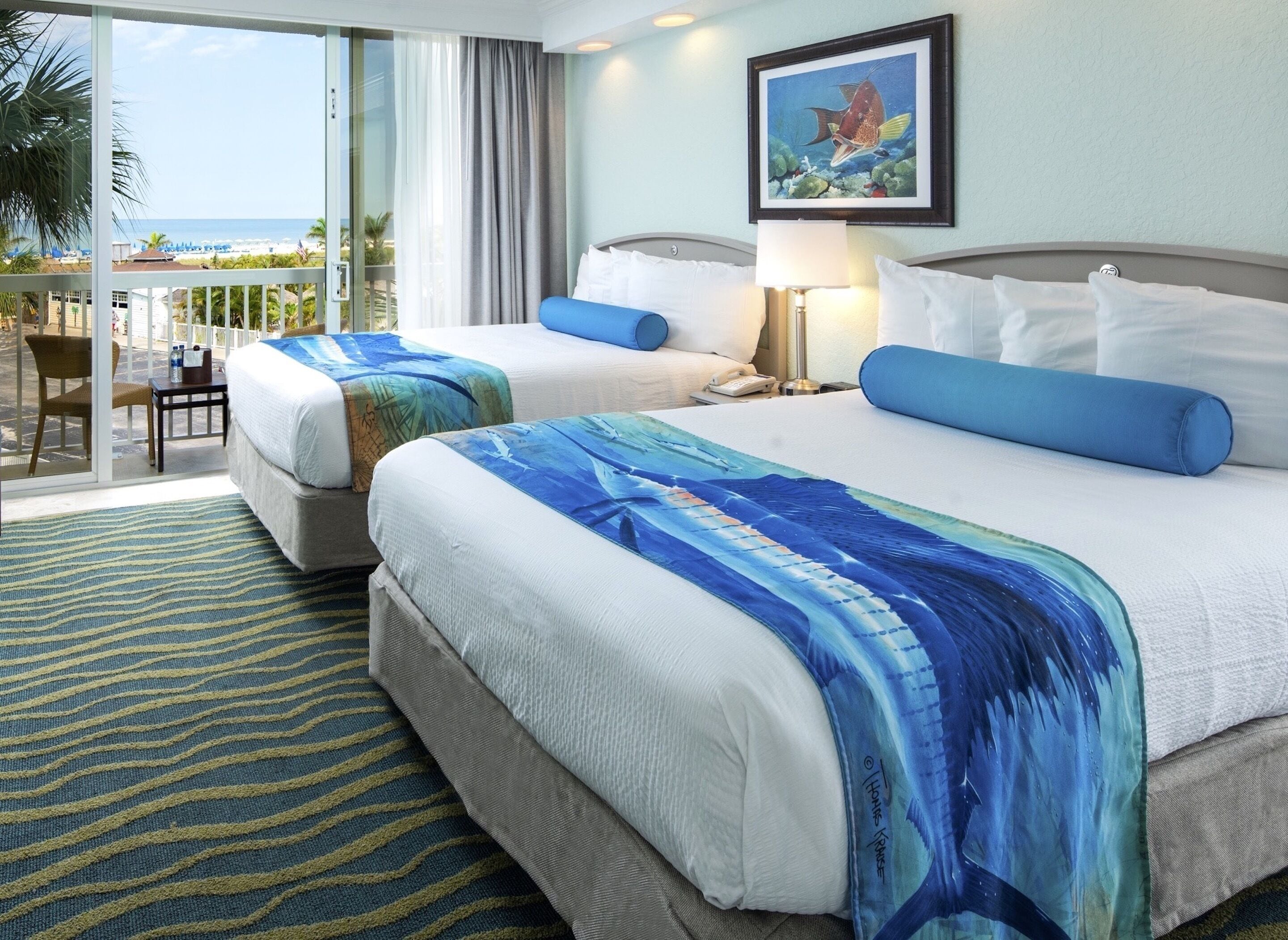 Habitación de hotel con dos camas, un balcón con vista a la playa y un cuadro en la pared.