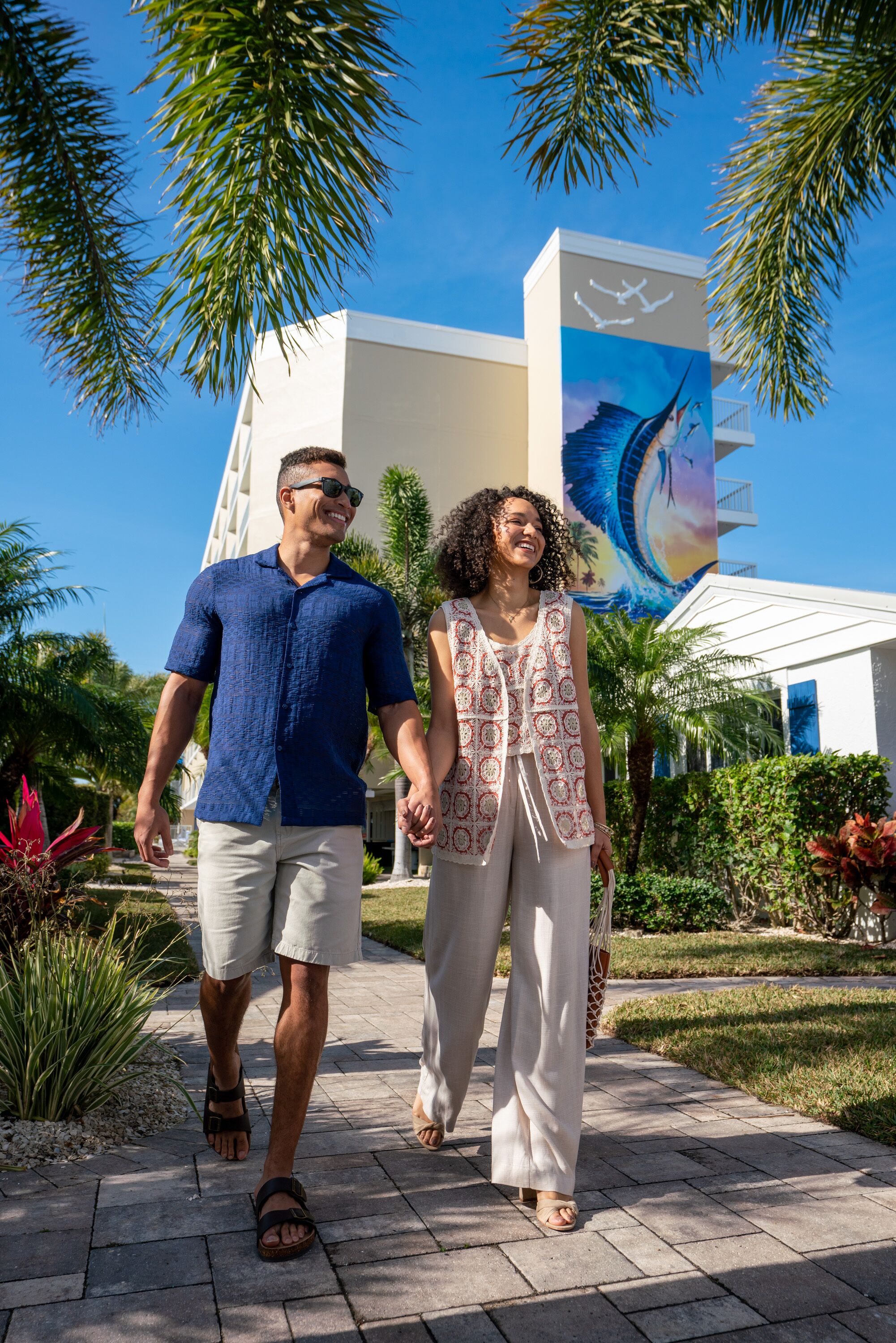 A couple walking on a paved pathway with a building featuring a mural in the background.