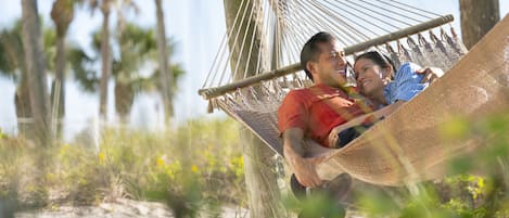 A hammock between two people in a natural setting with trees and grass.
