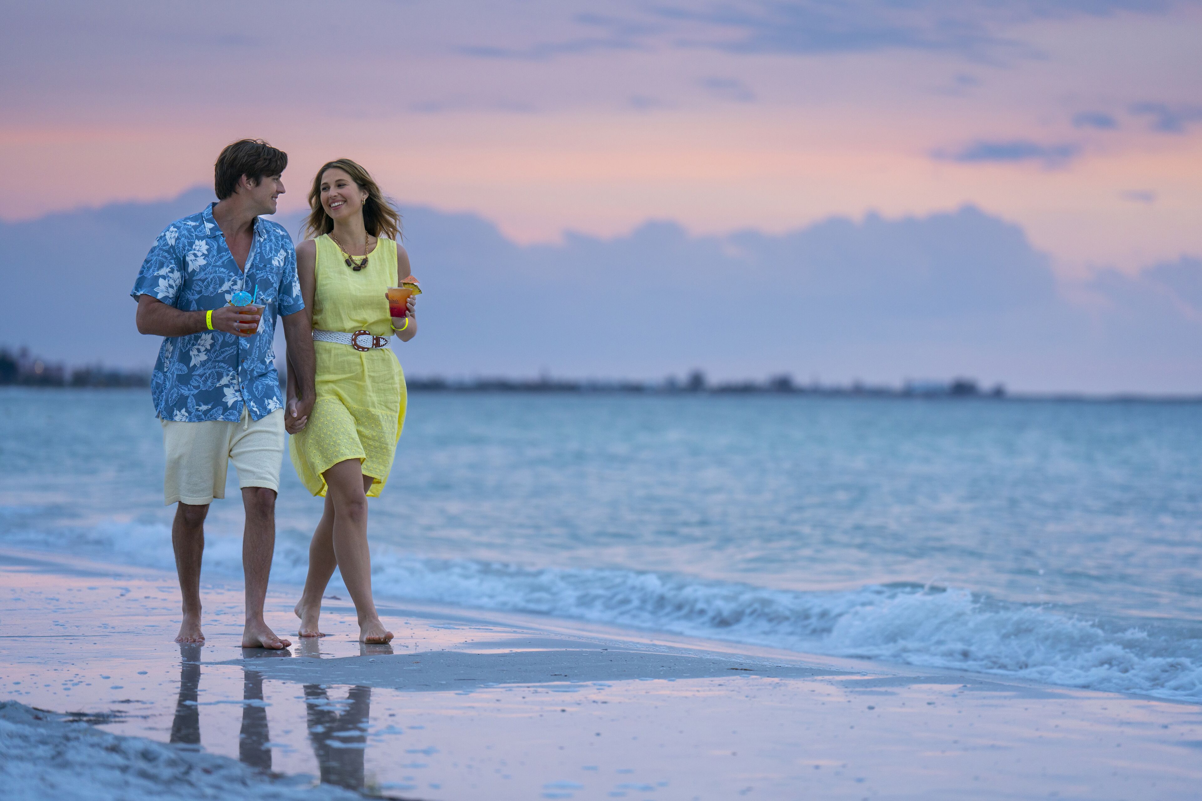 Un couple se promène sur une plage, avec un coucher de soleil en arrière-plan.