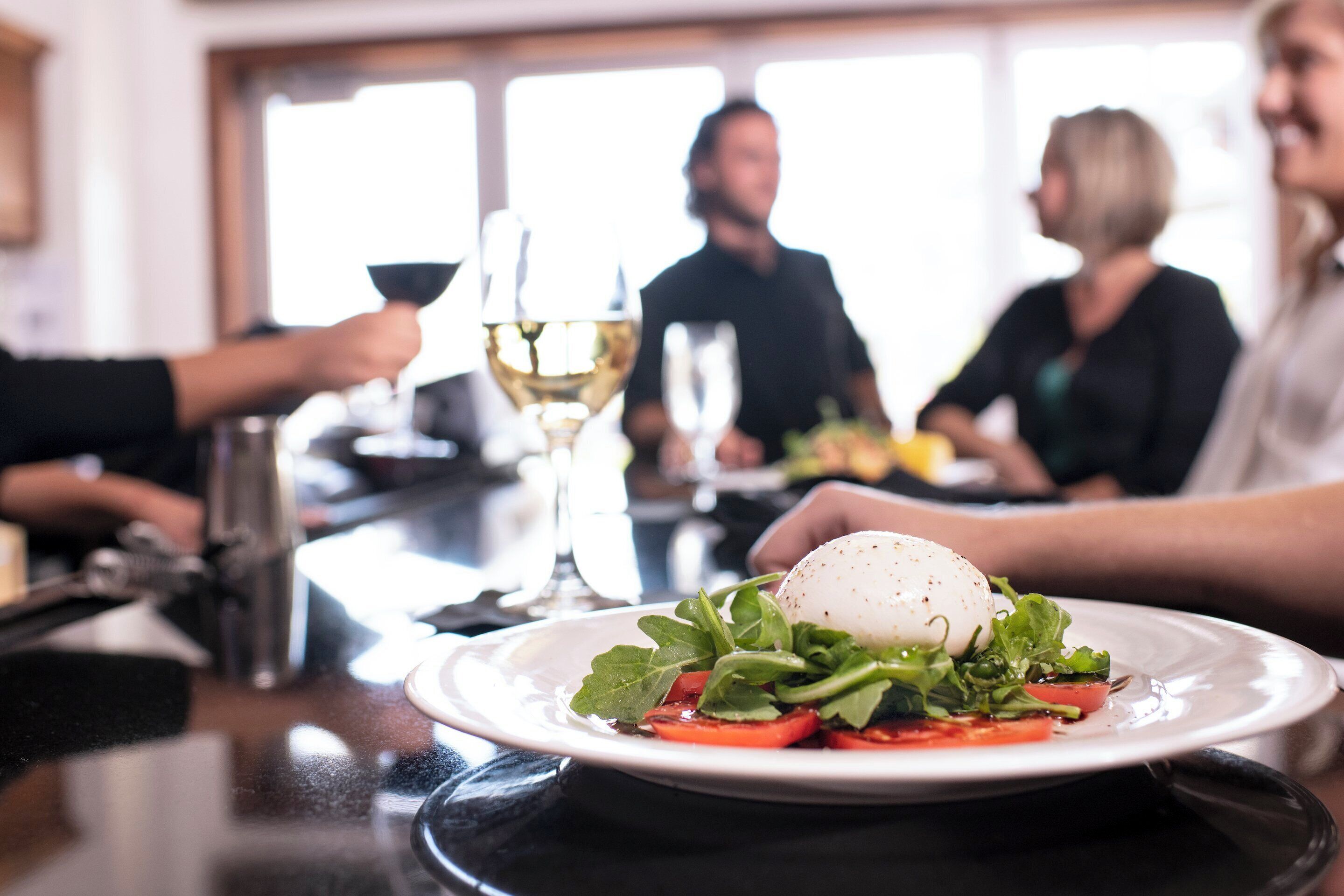 A dining table with a plate of food, a wine glass, and a person holding a glass.