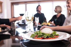 Un tavolo da pranzo con un piatto di cibo, un bicchiere di vino e una persona che tiene un bicchiere in mano.