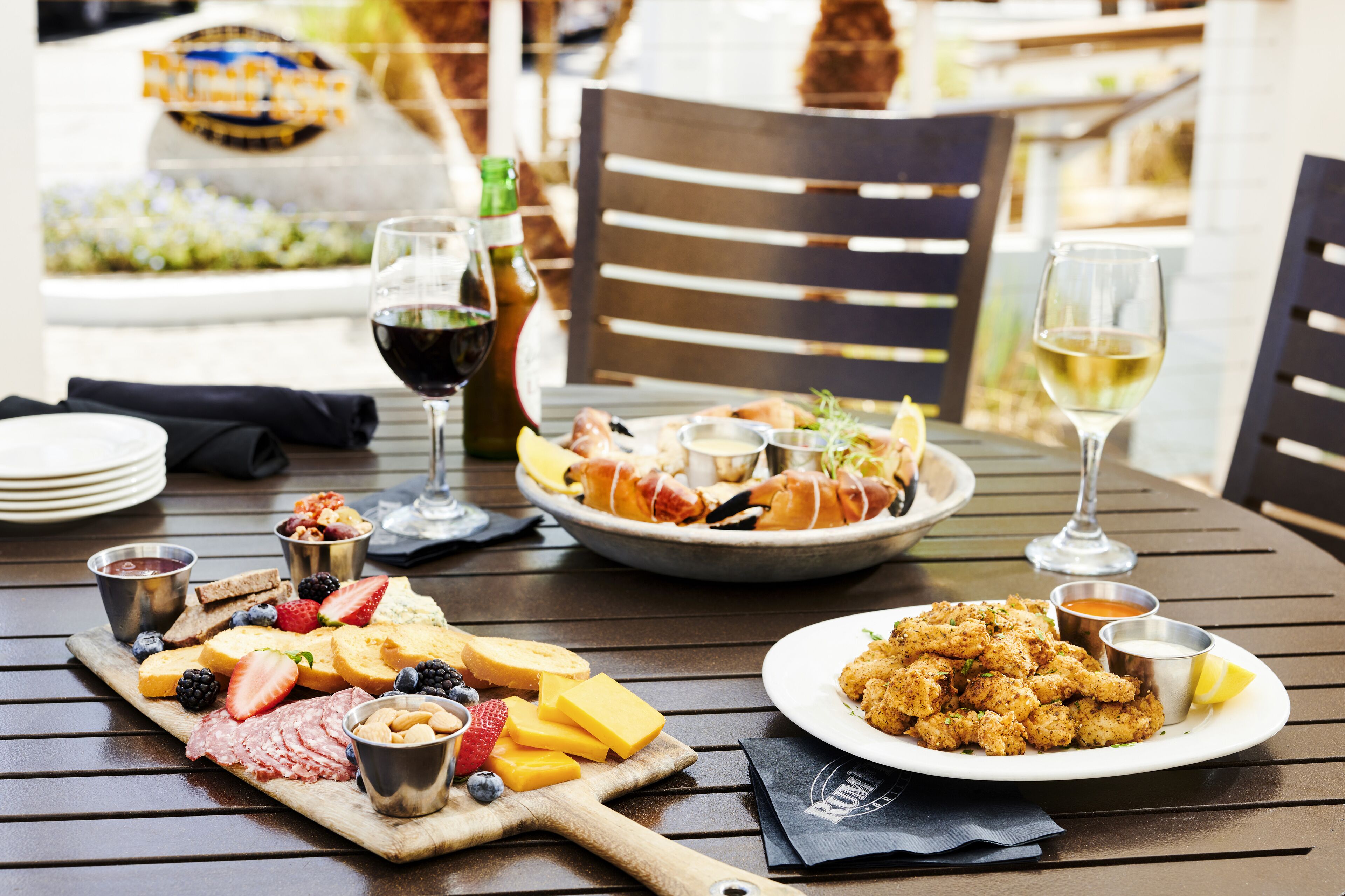 A dining table with a variety of foods including a charcuterie board, seafood, and bread. There are also glasses of wine and a bottle of beer.