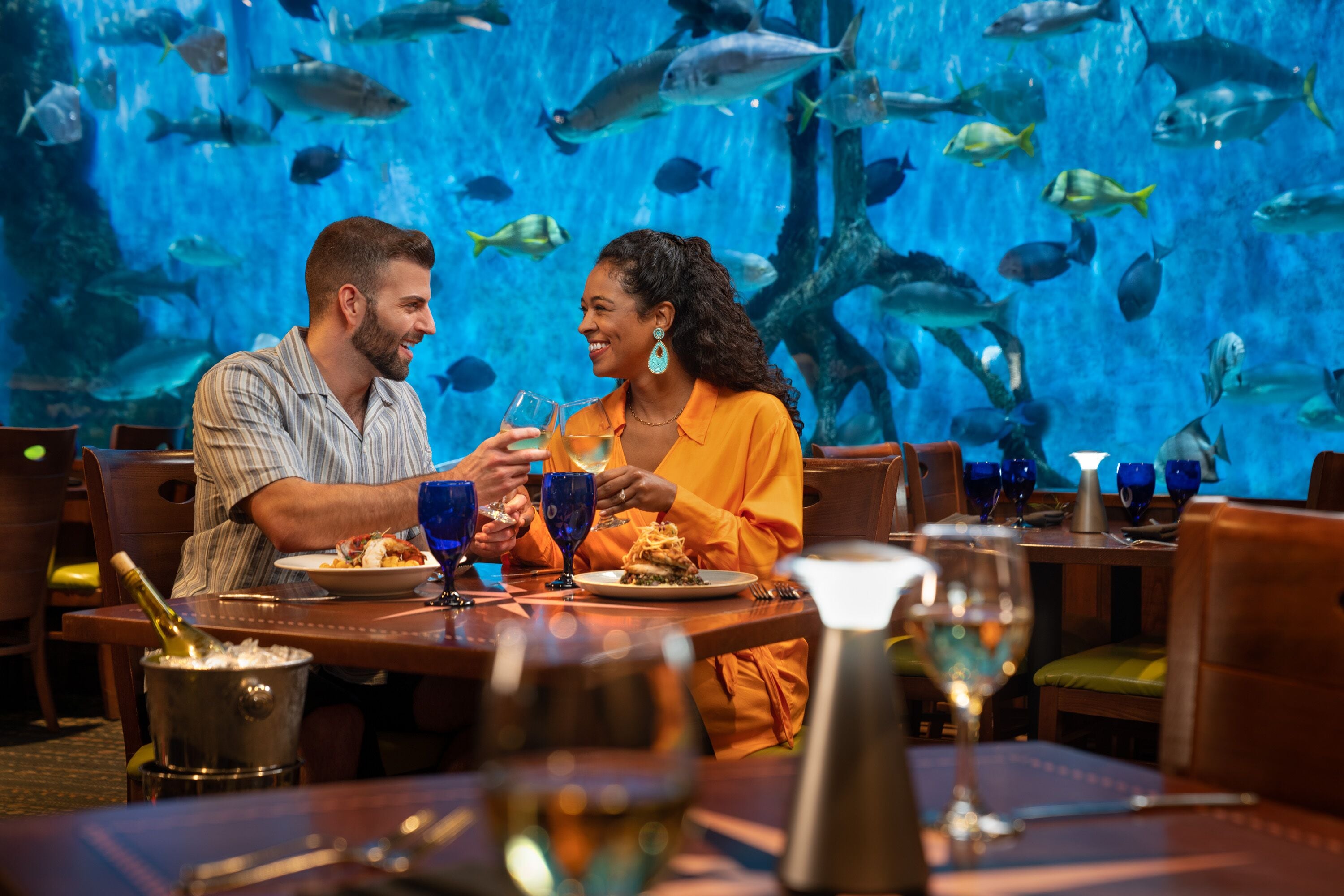Una pareja cenando en un restaurante con una pared de acuario al fondo.