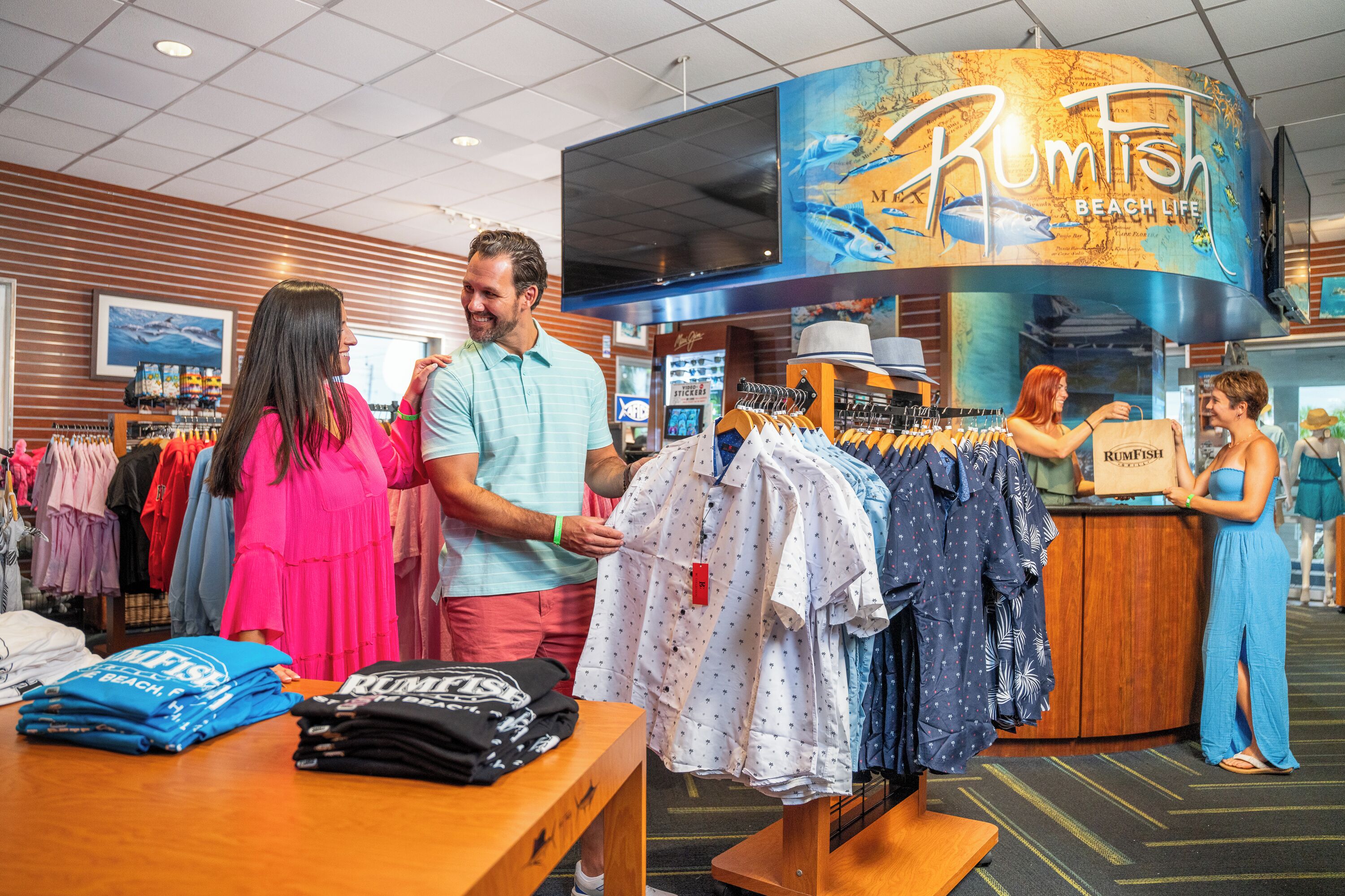 Een kledingwinkel met een opvallend bord met de tekst 'Rumfish Beach Life', rekken vol casual kleding en zwemkleding, en een toonbank met een 'Rumfish' tas.